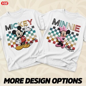 May include: Two white t-shirts featuring Mickey and Minnie Mouse. The Mickey shirt has a colourful checkered background with the word "MICKEY" in a 3D design. The Minnie shirt has a similar design with the word "MINNIE". Both shirts have character illustrations.
