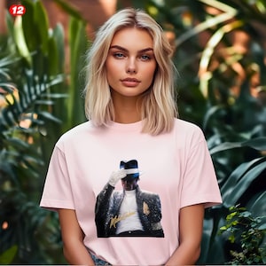 May include: A light pink t-shirt featuring a graphic of Michael Jackson in a black sequined jacket, white glove, and fedora. The image includes the text "Michael Jackson" in gold script. The background is a lush green foliage.