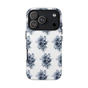 May include: A smartphone case featuring a white backdrop adorned with a repeating pattern of blue floral bouquets. The case incorporates a black camera module with three lenses and a flash. Designed to fit a mobile phone.