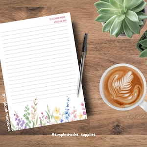 May include: A white sheet of lined stationery featuring a colourful watercolour floral border at the bottom. The paper includes the text TO LEARN MORE VISIT JW.ORG at the top and #1 - Blank Meadows on the side. A black pen rests on the paper.