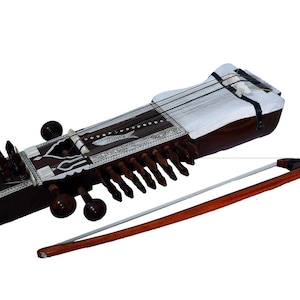 Puede incluir: Un sitar marrón con una parte superior blanca y detalles decorativos, acompañado de un arco de madera. El instrumento de cuerda presenta múltiples cuerdas y clavijas de afinación, ideal para la música clásica india.