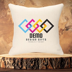 May include: Cream square cushion featuring a colourful geometric design and the text "DEMO DESIGN GIFTS". The cushion is displayed on a wooden tree trunk slice, creating a rustic look.