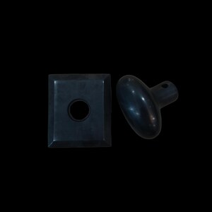 May include: A matte black door knob set consisting of a smooth, oval-shaped handle with a small side hole and a separate square-shaped mounting plate featuring a central circular opening. Both components have a dark, uniform finish.