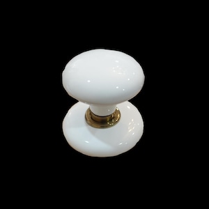 May include: A white ceramic door knob featuring a smooth, rounded handle and a matching circular base plate. The central connecting piece is made of a metallic brass-toned material, providing a contrast to the glossy white finish of the ceramic.