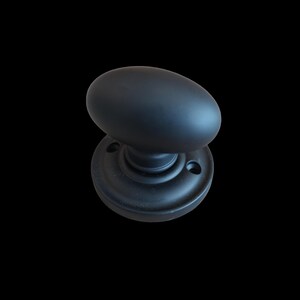 May include: A matte black oval door knob with a round base. The door knob is made of metal and has a classic design. The image is set against a black background.