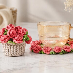 Peut inclure: Un ensemble au crochet composé d'un petit panier beige rempli de roses roses et de feuilles vertes, accompagné d'un dessous de verre circulaire assorti orné de roses roses et de feuilles vertes, supportant une tasse à thé en verre.