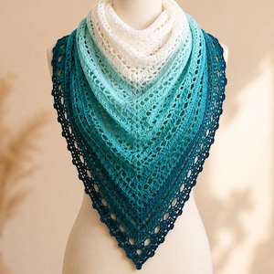 Peut inclure: Un châle triangulaire au crochet présentant un dégradé de couleurs allant du blanc au niveau du col au turquoise clair, au bleu sarcelle moyen, et enfin au bleu foncé profond sur le bord inférieur pointu, avec un motif en dentelle ajourée.