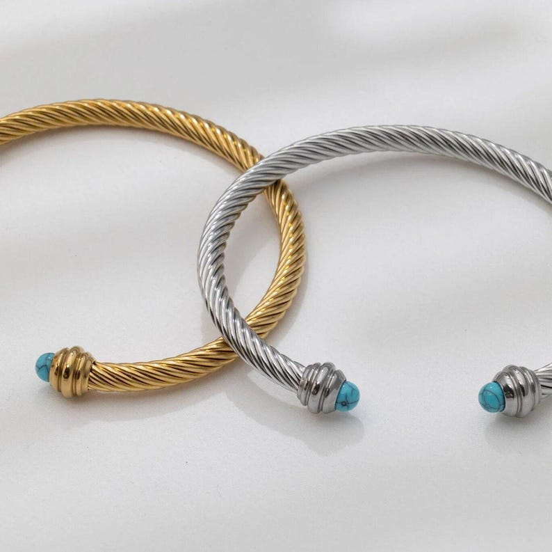 A gold twisted cuff bracelet and a silver twisted cuff bracelet with turquoise ends overlapping on a white surface.