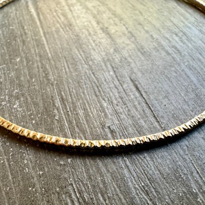May include: A gold-toned metal choker necklace with a textured, ridged design.