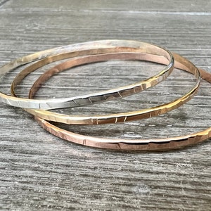 May include: Three hammered metal bangles in silver, gold, and rose gold.