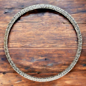 May include: A silver-colored metal hoop with an ornate design. The hoop is circular and has a smooth, polished finish. It is lying flat on a wooden surface.