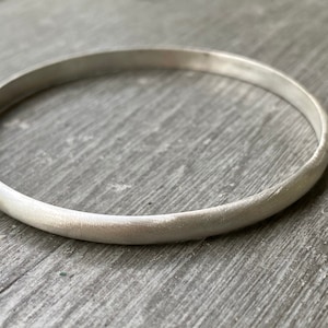 May include: A simple silver bangle bracelet with a smooth, brushed finish.