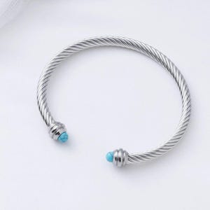 A single silver twisted cable cuff bracelet featuring turquoise beads on its ends, presented against a plain white background.