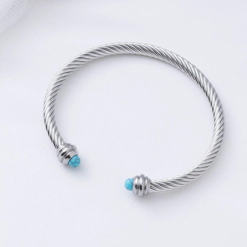 A single silver twisted cable cuff bracelet featuring turquoise beads on its ends, presented against a plain white background.