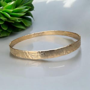 May include: A gold bangle bracelet with a hammered texture.