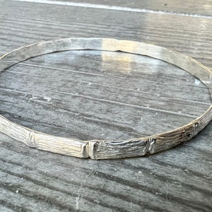 May include: A silver bangle bracelet with a textured, wood-like design.