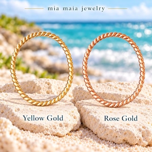 May include: Two thin, twisted metal rings, one in yellow gold and one in rose gold, are displayed. The text 'mia maia jewelry' appears at the top, with 'Yellow Gold' and 'Rose Gold' labels below each respective ring.