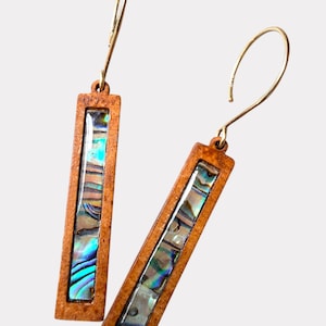 May include: A pair of rectangular earrings with a wooden frame and iridescent abalone shell inlay. The earrings have gold-colored ear wires. The abalone shell displays shades of blue, green, and brown.