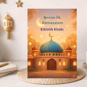 May include: A colorful book cover with a mosque illustration, a crescent moon, and stars. The text reads "Benim İlk Ramazanım Etkinlik Kitabı". The mosque has a blue dome and orange accents, set against a warm, glowing background.