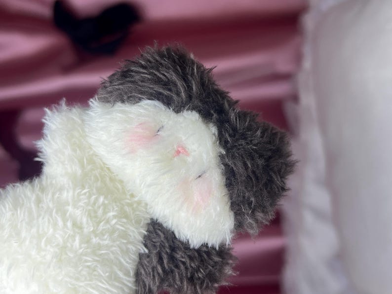 Peut inclure: Une peluche avec un design blanc et gris. Le jouet a une texture duveteuse, avec des accents roses sur les joues et les yeux ferm&eacute;s, sugg&eacute;rant un &eacute;tat de sommeil ou de d&eacute;tente. Le jouet est con&ccedil;u pour &ecirc;tre c&acirc;lin&eacute;.