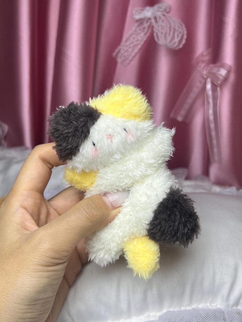 Peut inclure: Un jouet en peluche en forme de chat dans une pose c&acirc;line. Le jouet pr&eacute;sente un m&eacute;lange de fourrure blanche, jaune et noire. Le chat a de petites joues roses et est con&ccedil;u pour se donner l'impression de s'enlacer. Le jouet est doux et moelleux.