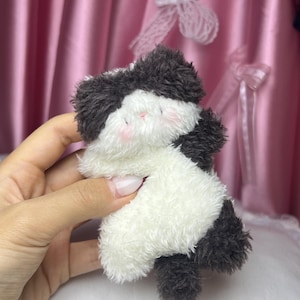 Peut inclure: Un petit jouet en peluche en forme de panda. Le panda est noir et blanc avec des joues roses. Le jouet est fait d'une mati&egrave;re douce et moelleuse et est tenu dans une main.