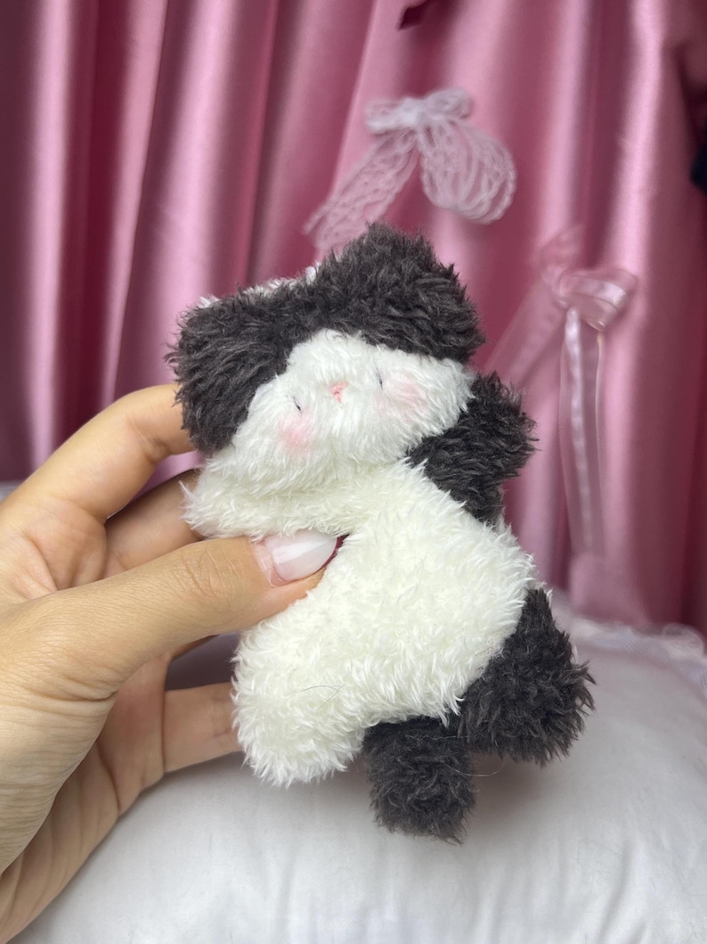 Peut inclure: Un petit jouet en peluche en forme de panda. Le panda est noir et blanc avec des joues roses. Le jouet est fait d'une mati&egrave;re douce et moelleuse et est tenu dans une main.