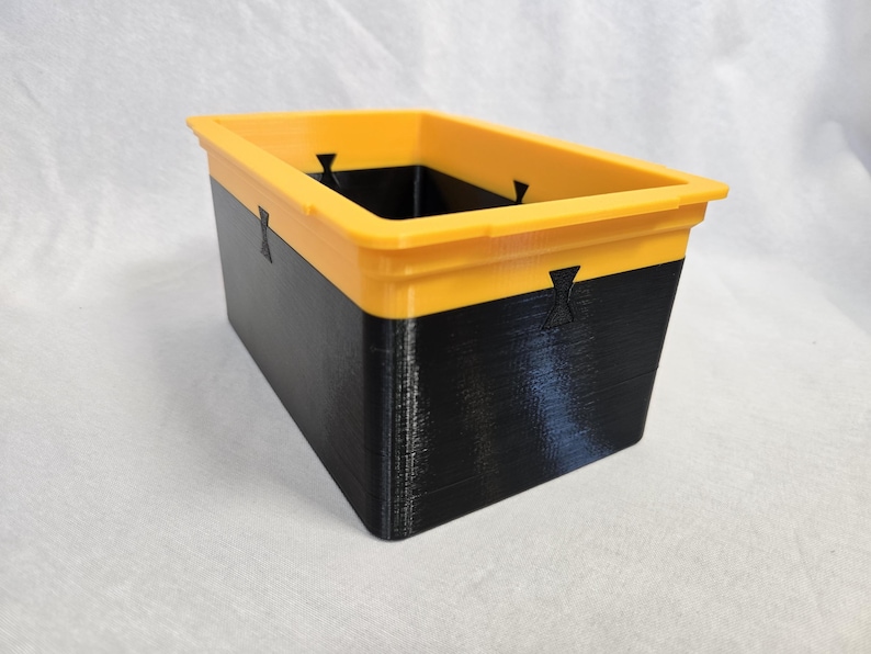 Puede incluir: Contenedor de almacenamiento rectangular de dos tonos. El borde superior es amarillo brillante y la secci&oacute;n inferior es negra. El contenedor tiene una superficie texturizada y probablemente est&aacute; hecho de pl&aacute;stico o un material similar.