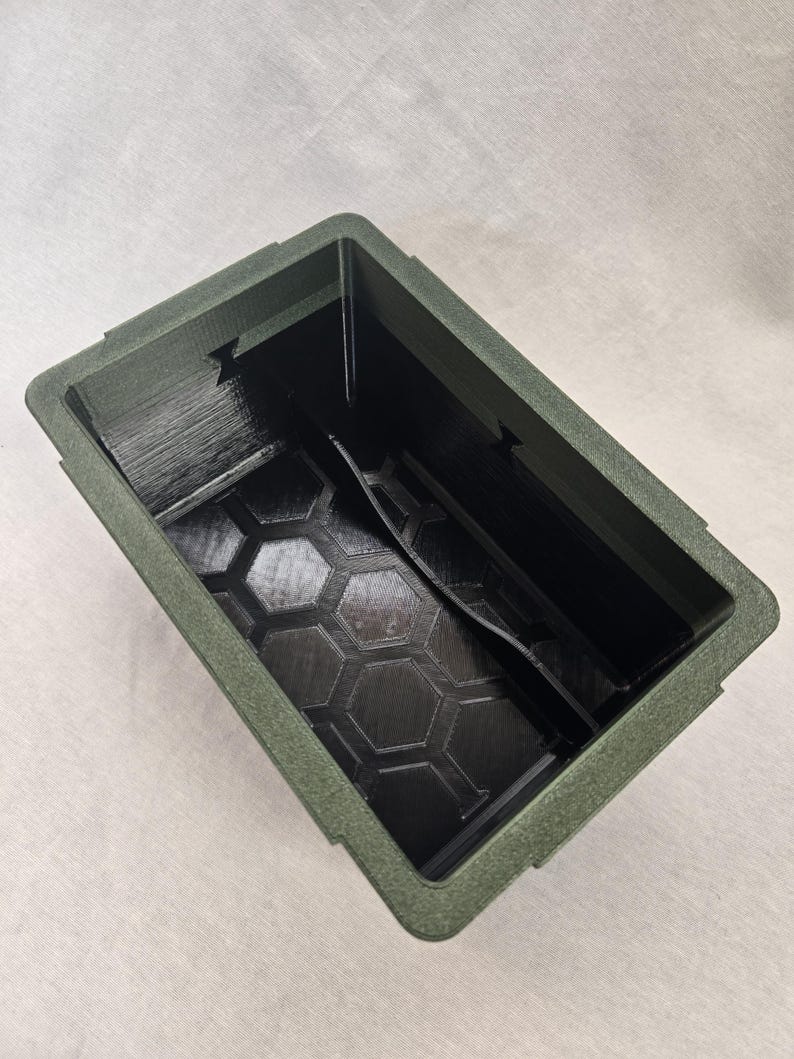 Puede incluir: Un contenedor rectangular verde oliva con un exterior texturizado y un interior negro. El interior presenta un patr&oacute;n de panal en la base y un divisor central. El contenedor est&aacute; vac&iacute;o y visto desde arriba.