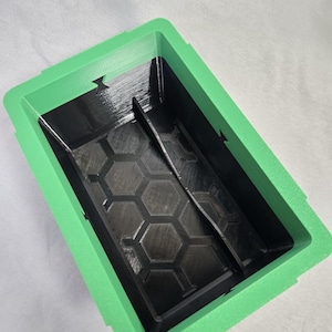 Puede incluir: Un contenedor rectangular de dos tonos con un marco verde y un interior negro. El interior presenta un patr&oacute;n de panal y un divisor central. El contenedor est&aacute; dise&ntilde;ado con una superficie texturizada.