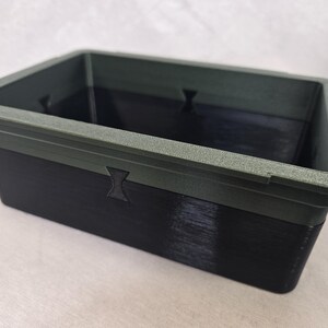 Puede incluir: Un contenedor rectangular de dos tonos. El borde superior es verde oscuro texturizado, mientras que la parte inferior es negra. El contenedor tiene un dise&ntilde;o simple y utilitario, con un acabado liso y una forma rectangular.