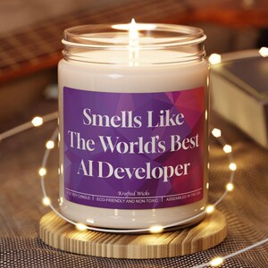 May include: A lit candle in a glass jar with a purple label that reads "Smells Like The World's Best AI Developer." The candle sits on a round wooden coaster. A guitar and a book are in the background.