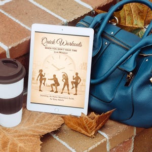Può includere: Un tablet bianco mostra il titolo "Quick Workouts" con sagome di esercizi. Una borsa a mano verde acqua, una tazza da viaggio bianca e marrone e una foglia caduta poggiano su una superficie di mattoni. L'immagine promuove il fitness e il benessere.