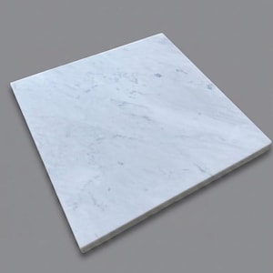 May include: A square slab of white marble featuring natural grey veining throughout the surface. The stone board has a smooth, polished finish and straight, clean edges, presenting a flat, uniform appearance with subtle variations in the grey patterns.