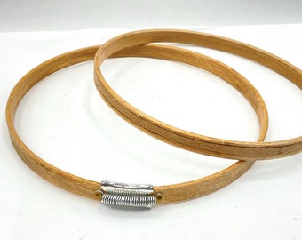 May include: Two wooden embroidery hoops, one nested inside the other. The hoops are made of natural wood and have a smooth finish. The smaller hoop has a metal tightening mechanism.