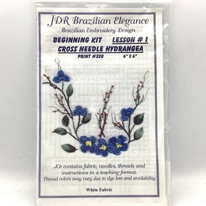 May include: A cross stitch embroidery kit featuring a blue hydrangea flower design. The kit includes fabric, needles, threads, and instructions. The kit is labeled "JDR Brazilian Elegance" and "Beginning Kit Lesson #1".