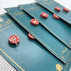 May include: Four cards with the text "The Button Collection" and "Hand painted in the USA" on them. Each card has a red button attached to it.