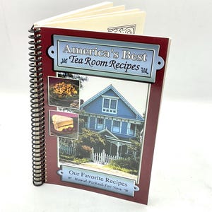 May include: A spiral-bound cookbook titled "America's Best Tea Room Recipes." The cover features a blue house, two food photos, and the text "Our Favorite Recipes Hand Picked For You." The book has a burgundy border and a black spiral binding.