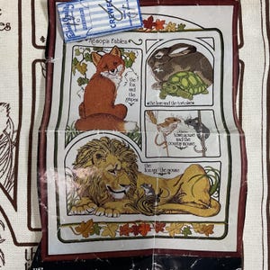 May include: A vintage fabric panel featuring illustrations from Aesop's Fables. The panel includes images of a fox, a rabbit, a tortoise, a lion, and mice. The text "Aesop's Fables" is visible at the top. A small packet of needles is attached.