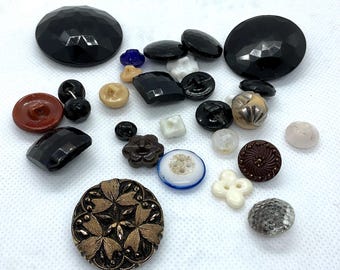 May include: A collection of various vintage buttons in different shapes, sizes, and colors. Includes black faceted buttons, brown, beige, and white buttons, and a large ornate button with gold and bronze detailing. Ideal for sewing and craft projects.