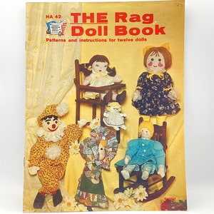 May include: The cover of a vintage book titled "THE Rag Doll Book" with a yellow background and illustrations of rag dolls. The book cover features the text "Patterns and instructions for twelve dolls".