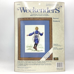 May include: A cross stitch pattern featuring a girl in a blue dress and white apron skipping in a field. The pattern is titled "Skippin' Gambade" and is part of the Weekenders collection. The kit includes 100% cotton Aida fabric, presorted 100% cotton floss, a needle, a designer mat, and complete instructions.