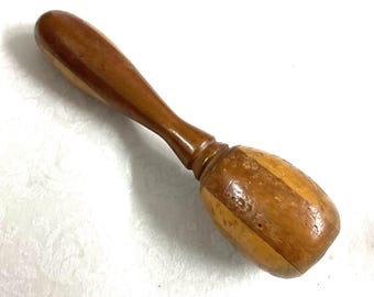 May include: A wooden muddler with a light brown handle and a darker brown, striped head. The muddler is made of polished wood and has a smooth, ergonomic design. It is likely used for mixing cocktails or other beverages.