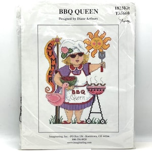 May include: A cross-stitch kit featuring a cartoon image of a woman in a chef's hat and sunglasses, holding a watermelon and a spatula. The design includes a flamingo, a grill, and the words "BBQ Queen" and "Summer".