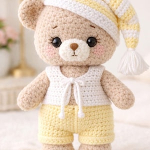 May include: A handmade crochet teddy bear wearing a white and yellow striped nightcap, a white vest, and yellow shorts. The bear has a light brown body, rosy cheeks, and black eyes. A cute, soft toy for children.