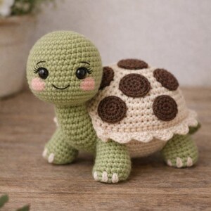 Puede incluir: Una tortuga de ganchillo hecha a mano en tonos verdes, crema y marrón. La tortuga tiene una cara sonriente con mejillas rosadas y pestañas. El caparazón presenta lunares marrones. Un juguete suave y encantador para niños.