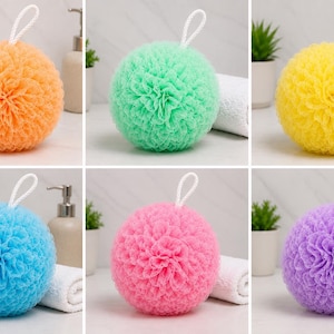 Peut inclure: Un ensemble de six éponges de bain sphériques en orange, vert clair, jaune, bleu clair, rose et violet. Chaque éponge en maille présente une texture dense et froncée avec une boucle de suspension blanche fixée au sommet.