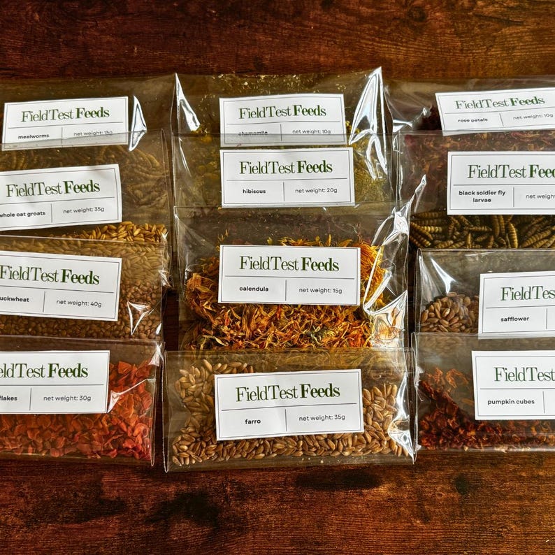 Puede incluir: Una colecci&oacute;n de bolsas de pl&aacute;stico transparente llenas de varios ingredientes secos, cada una etiquetada como "Field Test Feeds". Los ingredientes incluyen gusanos de la harina, avena entera, trigo sarraceno, copos, farro, cal&eacute;ndula y c&aacute;rtamo. Los pesos netos se indican en gramos.