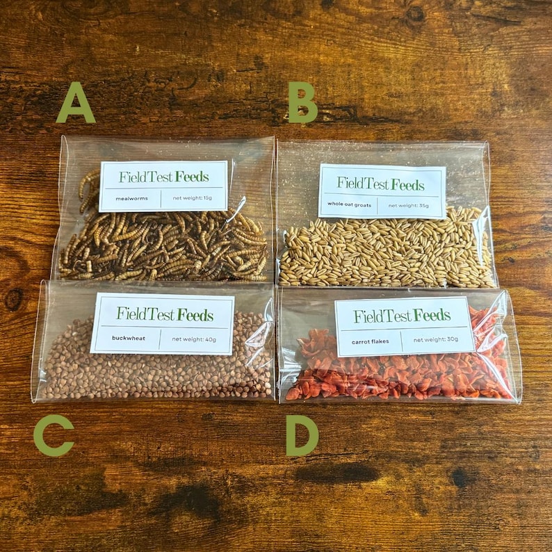 Puede incluir: Cuatro bolsas transparentes de comida para mascotas se muestran sobre una superficie de madera. Las bolsas contienen gusanos de la harina, granos de avena entera, trigo sarraceno y copos de zanahoria. Cada bolsa tiene una etiqueta que dice "FieldTest Feeds".