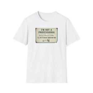 May include: A white short-sleeve t-shirt featuring a rectangular graphic on the chest. The graphic resembles a vintage sign with the text: I'M NOT A PROFESSIONAL. But if you tell me your problems I'LL TRY TO SOLVE THEM FOR YOU! with a small icon.